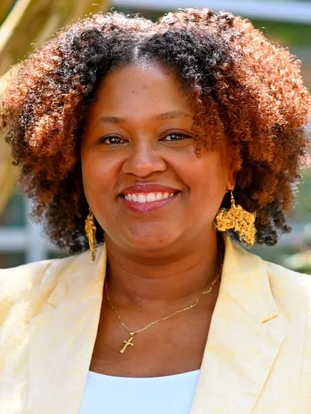 Black woman with brown hair smiling wearing a yellow blazer