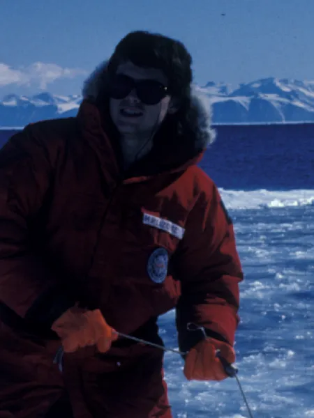 Person wearing a red winter coat and red gloves with sunglasses on, standing with ice all around them.