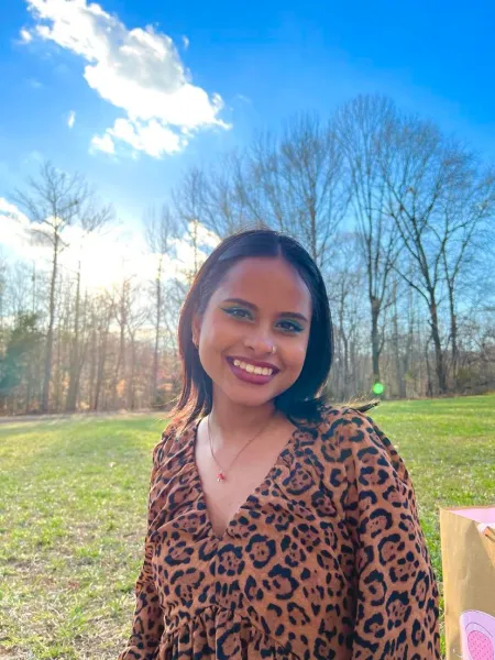 Woman with short black hair smiling widely wearing a cheetah print long sleeve shirt