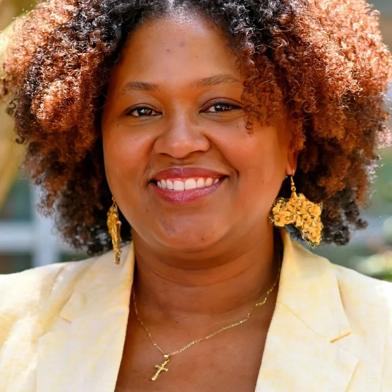 Black woman with brown hair smiling wearing a yellow blazer