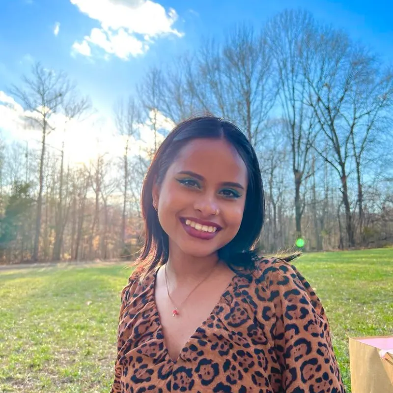 Woman with short black hair smiling widely wearing a cheetah print long sleeve shirt