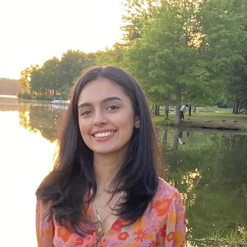 Woman wearing a floral orange top with straight black hair smiling and looking at the camera